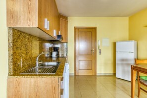 Une cuisine dotée de plans de travail en granit, d’armoires en bois, d’un évier en acier inoxydable, d’une machine à café, d’un réfrigérateur et d’une porte en bois.