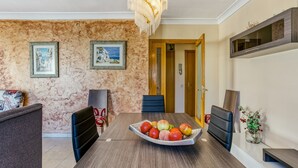 A dining area with a wooden table, chairs, a chandelier, framed artwork on the walls, and a door leading to another room. - Apartment 'La Cargolera' with Sea View, Balcony and Wi-Fi (La Escala)