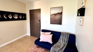 Una sala de estar con un sofá azul oscuro, una puerta y un cuadro colgado en la pared que muestra un paisaje montañoso.