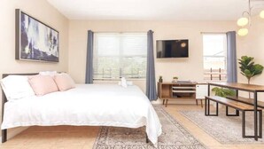 Un dormitorio con cama, escritorio, televisión y ventana con cortinas.