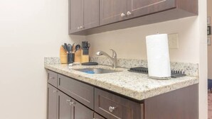 Una cocina con encimeras de granito, un lavamanos de acero inoxidable y armarios de madera.
