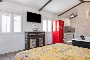 Une chambre avec un lit, une télévision, une armoire rouge, un coin cuisine et une salle de bain.