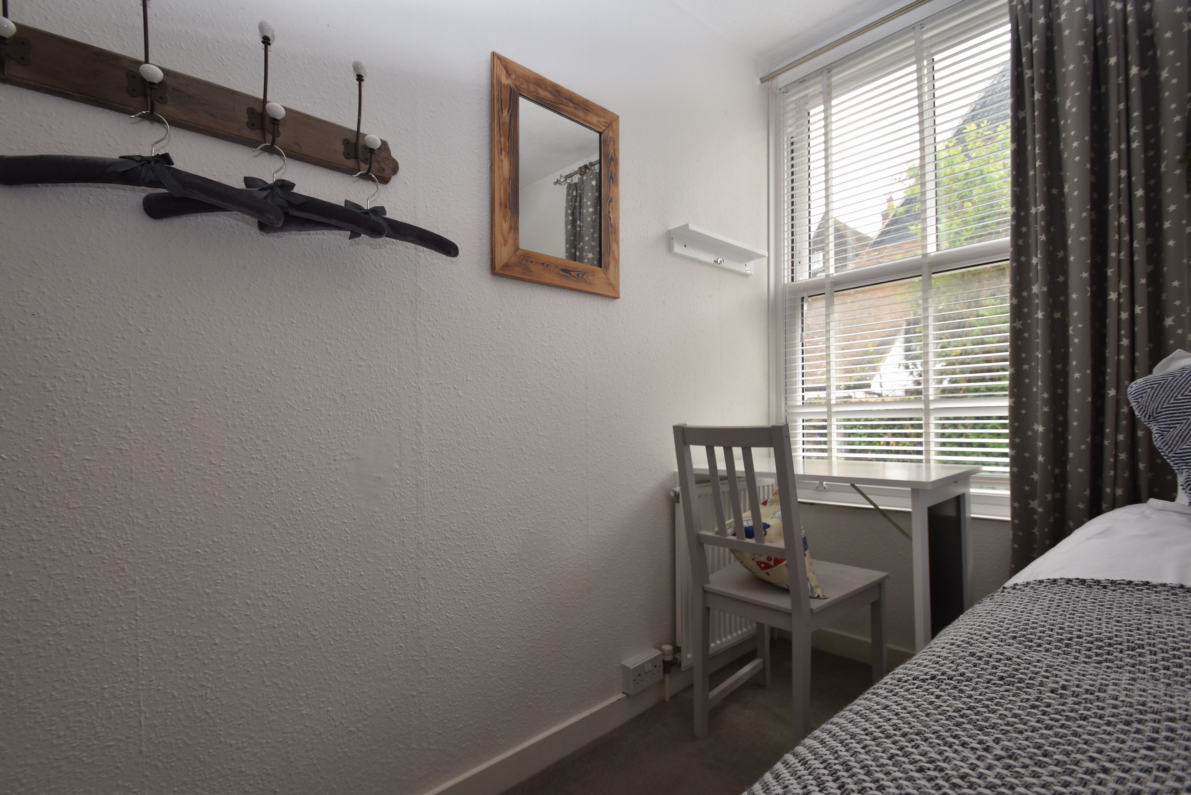 Een slaapkamer met een bed, een stoel, een klein tafeltje, een spiegel en een kapstok.