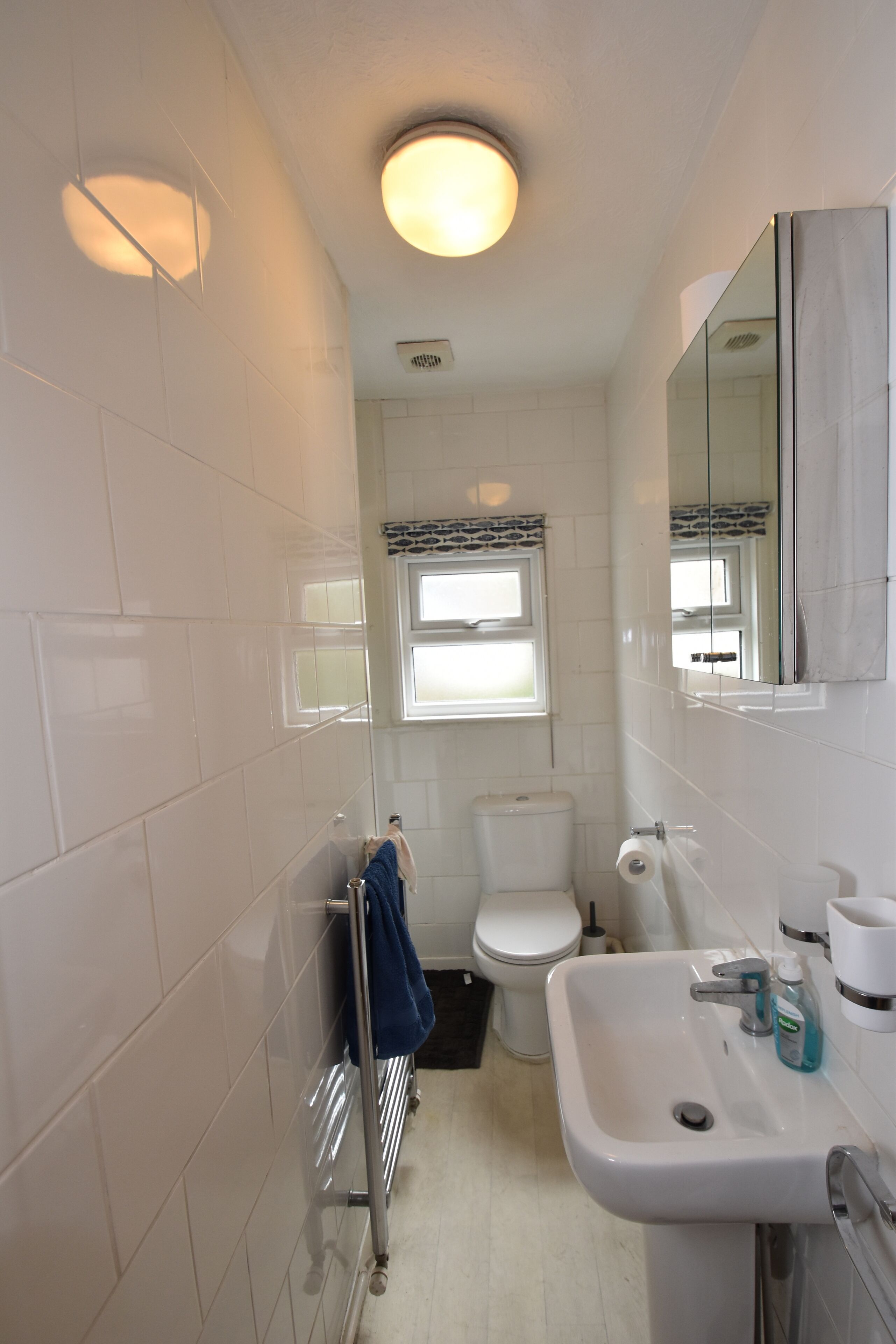 Une petite salle de bain avec des carreaux blancs, des toilettes, un lavabo avec un miroir et un porte-serviettes.