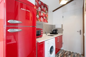 Une cuisine compacte équipée d’un réfrigérateur rouge, d’un four à micro-ondes, d’une machine à café et d’un lave-linge.