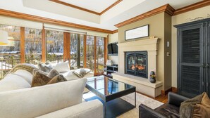 A cozy living room with a fireplace, large windows, and comfortable seating. - Exceptional Ritz-Carlton Residence by InvitedHome | Ski Valet, Pool, Hot Tub (Vail)