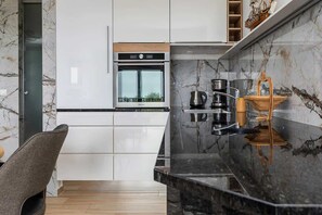 A modern kitchen with white cabinetry, a built-in oven, and a marble backsplash.