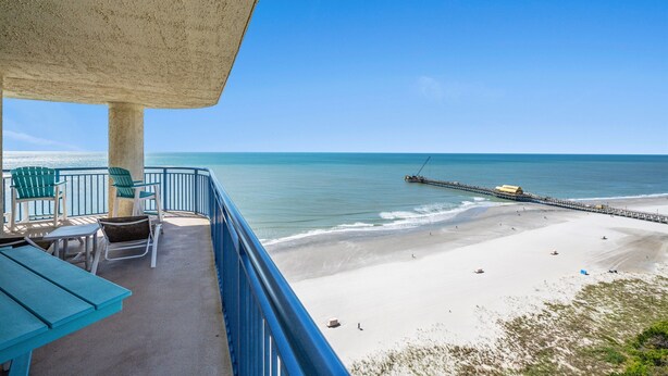 Ein Balkon mit Stühlen und Tisch, der Blick auf einen Strand und einen Steg bietet.