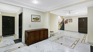A spacious hallway with marble flooring, a wooden cabinet, and a staircase leading to another level. - Itsy Hotels Arien International (New Delhi)