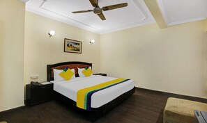A hotel room with a bed, a nightstand, a telephone, a ceiling fan, and a picture on the wall.