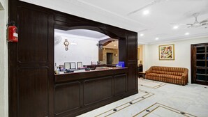 A reception area with a dark wooden desk, a clock, and a framed certificate. - Itsy Hotels Arien International (New Delhi)