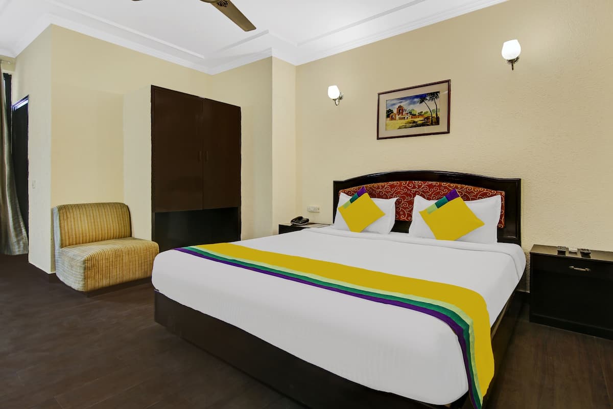 A hotel room with a large bed, a chair, a nightstand, a phone, and a painting on the wall.