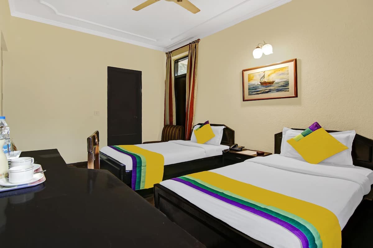 A hotel room with two beds, a desk with a telephone, a water bottle, and a pitcher.