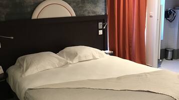A neatly made bed with white linens in a room with a dark headboard, a red curtain, and a visible bathroom door.