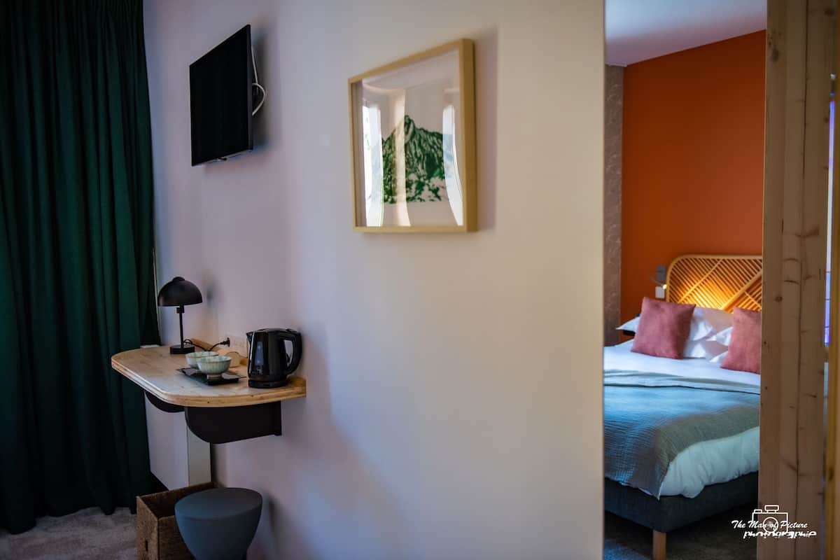 Habitación de hotel con cama, escritorio con lámpara, un cuadro enmarcado y televisor en la pared.