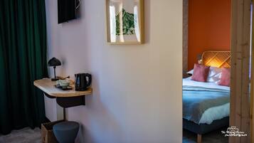 Habitación de hotel con cama, escritorio con lámpara, un cuadro enmarcado y televisor en la pared.