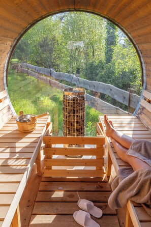Una terraza de madera con un ventanal circular que da a un área verde y una cerca de madera.