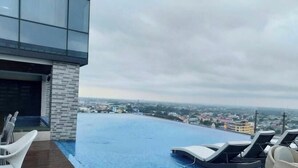 An infinity pool with lounge chairs, a wooden deck, and a city view. - Luxurious 1 Bedroom King Bed Skyline View Walking Street Condo (Angeles)
