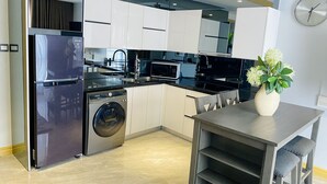 A modern kitchen with stainless steel appliances, a built-in washing machine, and a dining area with a vase of flowers. - Luxurious 1 Bedroom King Bed Skyline View Walking Street Condo (Angeles)