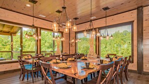 A large wooden dining table with chairs, surrounded by large windows with blinds, and hanging pendant lights. - Dreamers Mountain Retreat: Pool, Theater, Hot Tub, WiFi, Games, Fire Pit (Sevierville)