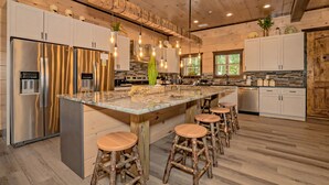 A modern kitchen with a large island, bar stools, stainless steel appliances, and wooden accents. - Dreamers Mountain Retreat: Pool, Theater, Hot Tub, WiFi, Games, Fire Pit (Sevierville)
