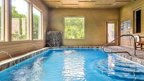 An indoor swimming pool with clear water, a stone wall, and a view of greenery outside. - Dreamers Mountain Retreat: Pool, Theater, Hot Tub, WiFi, Games, Fire Pit (Sevierville)