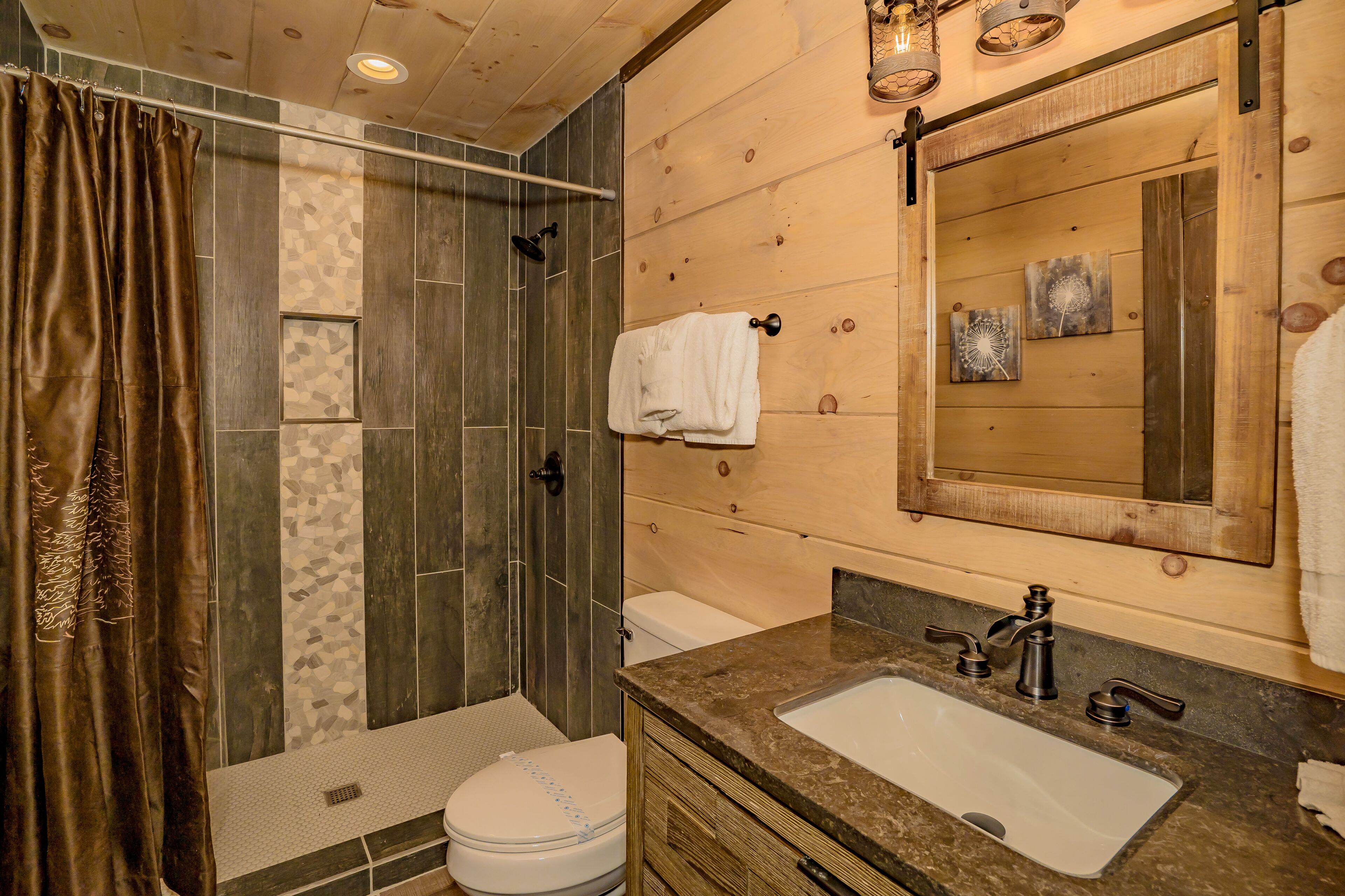 Un baño con ducha, inodoro, lavabo y paredes de madera.