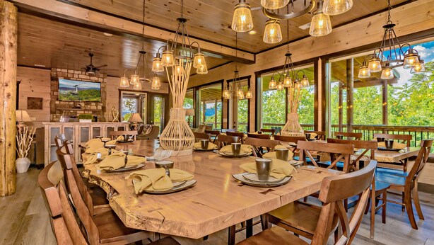 A wooden dining area with a large table, chairs, and hanging light fixtures. - Dreamers Mountain Retreat: Pool, Theater, Hot Tub, WiFi, Games, Fire Pit (Sevierville)