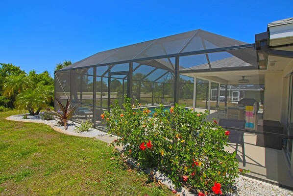 A covered outdoor area with a pool, surrounded by a glass enclosure, and a garden with various plants and flowers.