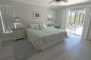 A bedroom with a bed, a nightstand, a lamp, a window with curtains, and a view of the outdoors.