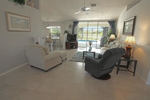 A living room with a sofa, armchair, TV, and a dining area with chairs and a table.