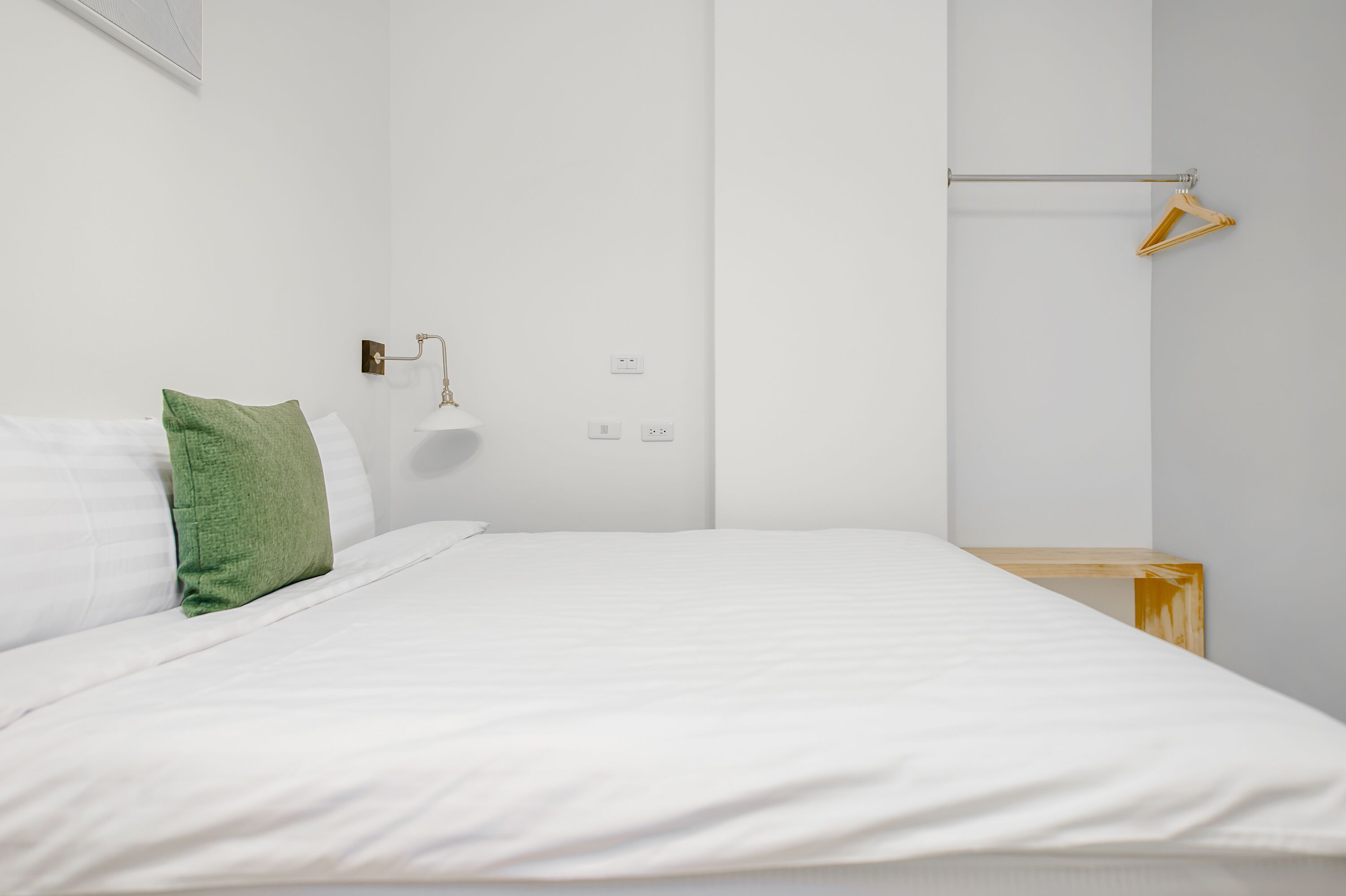 Un dormitorio minimalista con cama, mesita de noche, lámpara de pared y perchero.