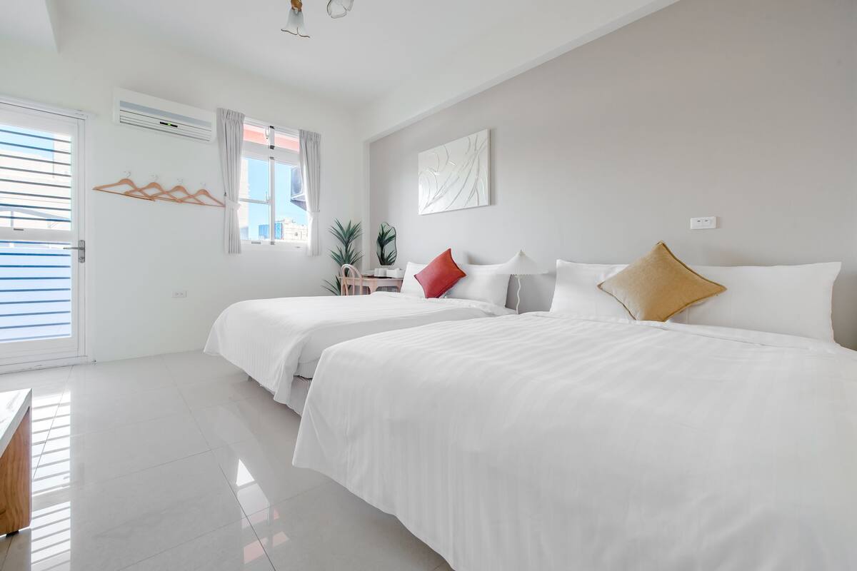 Habitación de hotel con dos camas, una ventana con cortinas, aire acondicionado instalado en la pared y una mesita con una planta.