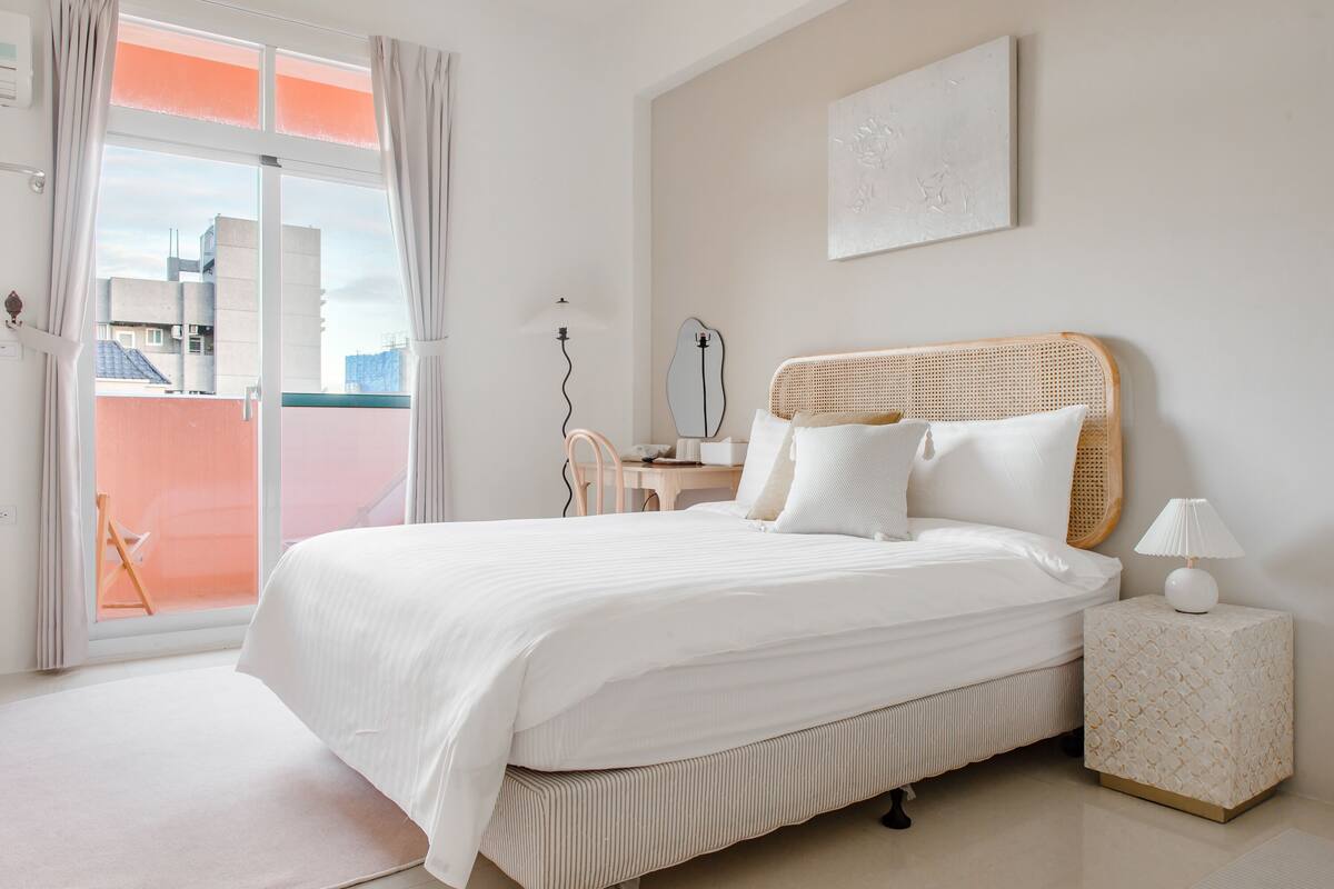Un dormitorio ordenado con una cama grande, una mesita de noche y vistas a un balcón exterior por una puerta corrediza.