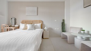 A modern bedroom with a large bed, a bedside table with a lamp, a small side table, a wicker chair, a round coffee table, and a cactus plant. - Pet Friendly Taitung Chun Yang Smart Stay (Taitung)