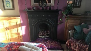 Een kamer met een open haard, een bed met een kleurrijk sprei, een stoel met een decoratief kussen en een kleine tafel met een plant.