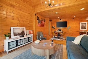Una habitación acogedora de estilo cabaña con paredes de madera, televisor, comedor y sofá.