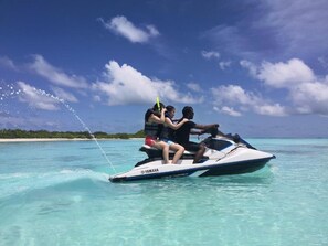 A jet ski with three people on it, moving through clear turquoise water. - Xen Midu (Hulhudhoo)