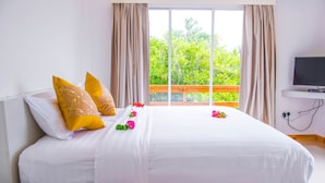 Una cama bien hecha con almohadas blancas y amarillas, un control remoto en un estante y un televisor sobre un mueble.