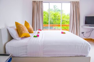 Una cama bien hecha con almohadas blancas y amarillas, un control remoto en un estante y un televisor sobre un mueble.