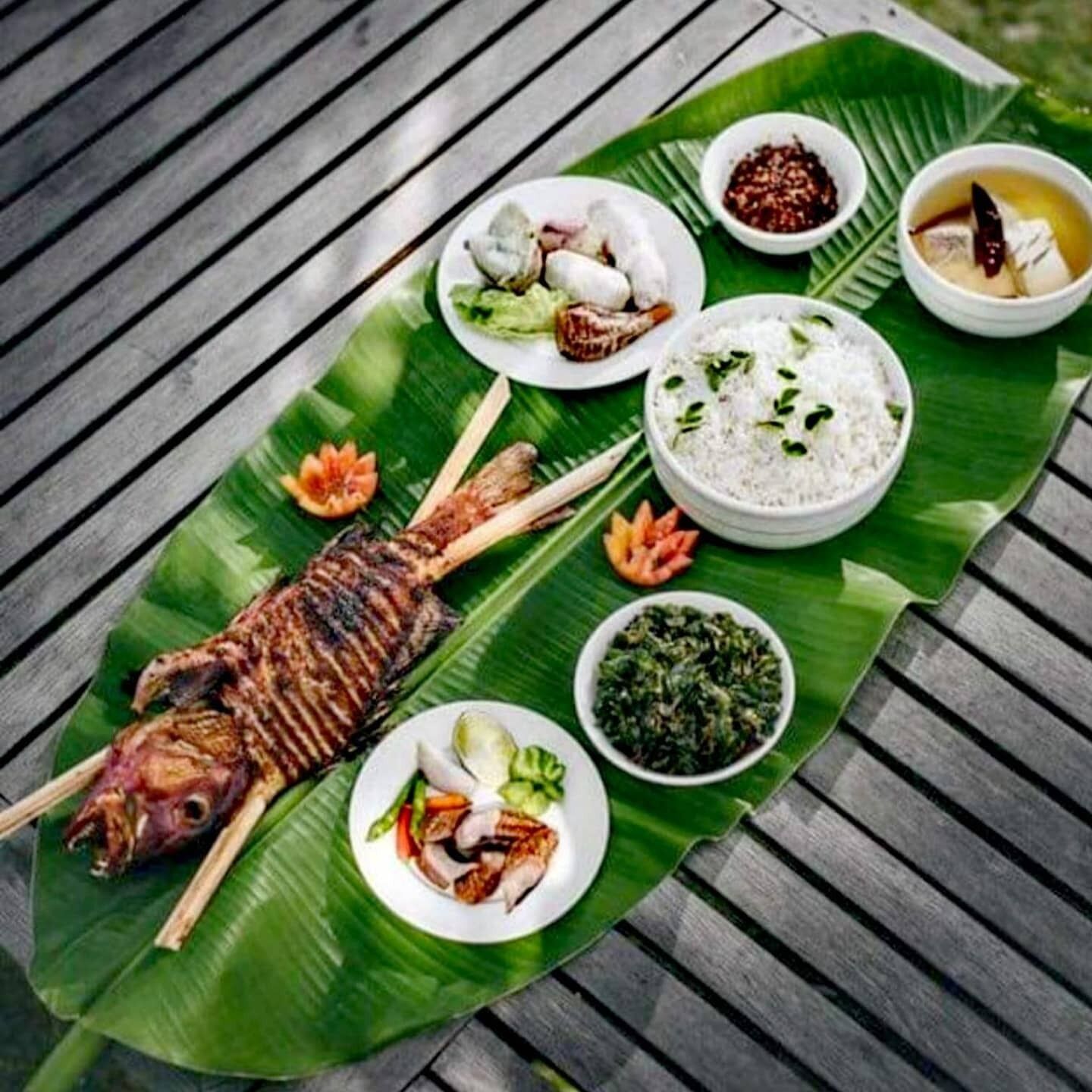 A meal served on a banana leaf with grilled fish, rice, and various side dishes.