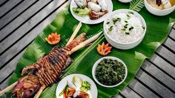 A meal served on a banana leaf with grilled fish, rice, and various side dishes.
