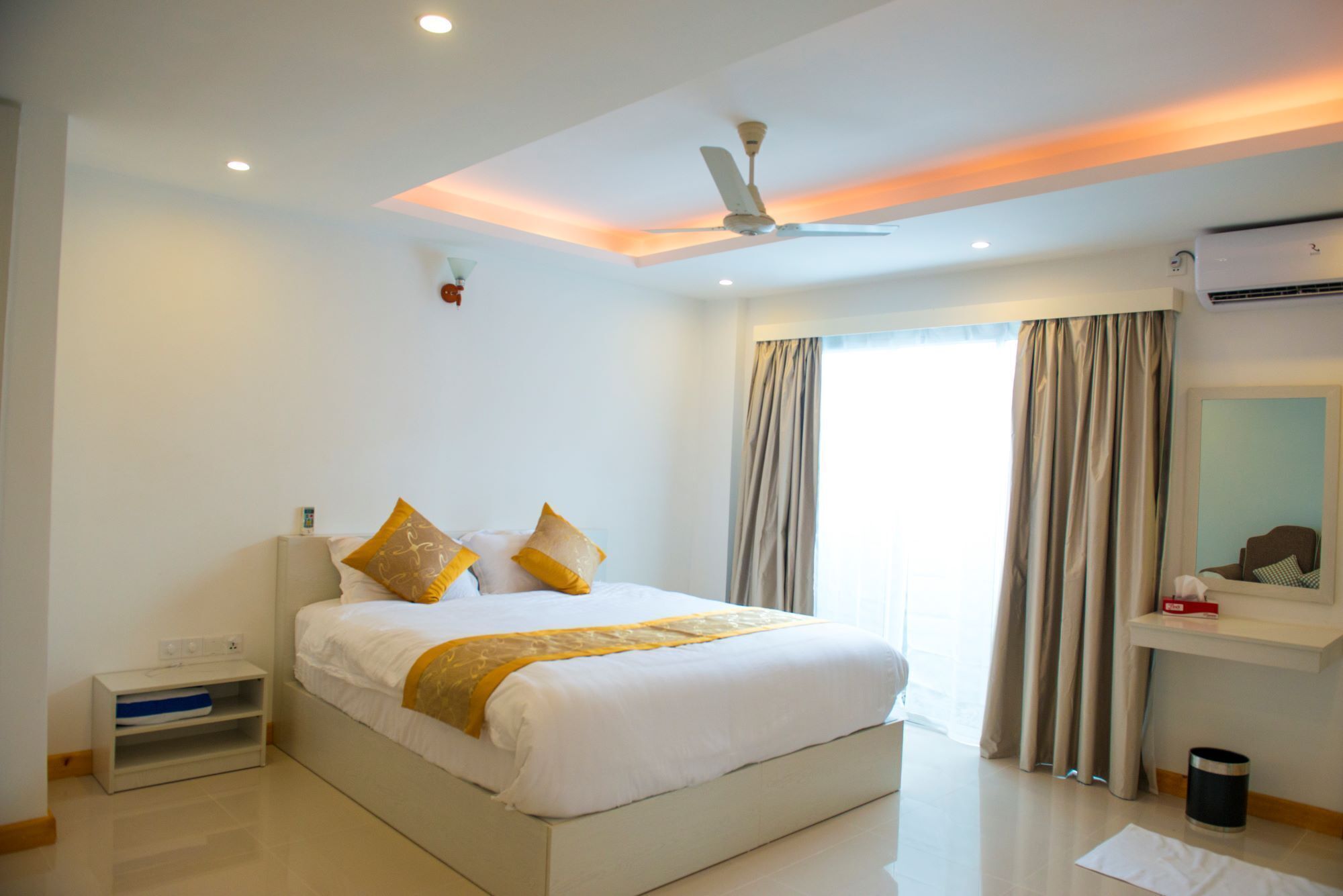 Una habitación de hotel moderna con una cama grande, un ventilador de techo y un ventanal con cortinas.