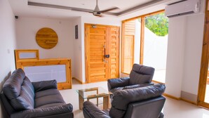 Una sala de estar moderna con dos sofás de cuero, una mesa de centro de vidrio, puertas de madera y un ventilador de techo.