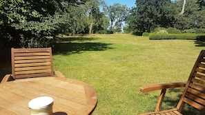 A wooden table and chairs in a well-maintained grassy area with trees in the background.