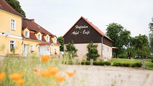 A building with a sign reading "Hofladen Apfel - Café" surrounded by greenery and a field of poppies. - Uckermark-Im Gutshaus vacation apartment (Boitzenburger Land)