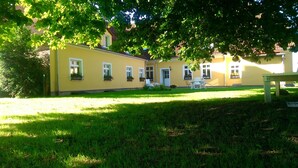 A yellow building with multiple windows, a door, and a small lawn area with a bench. - Uckermark-Im Gutshaus vacation apartment (Boitzenburger Land)