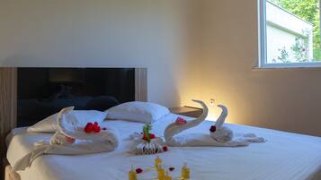 A neatly made bed with white linens, a bouquet of red roses, and two swan-shaped towels.