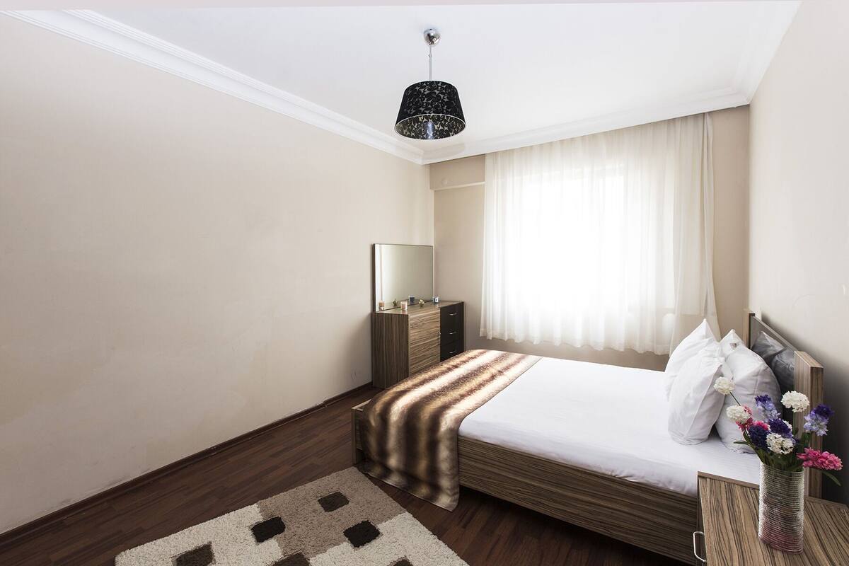 Une chambre d’hôtel équipée d’un lit, d’une table de chevet, d’un miroir et d’un luminaire suspendu.