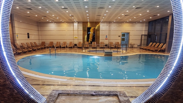 Ein großer Innenpool mit einem runden Rundgang, umgeben von Liegestühlen und einem roten Teppich, der zum Pool führt.
